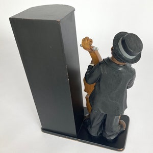 Pu&ograve; includere: Un fermacarte nero e marrone con una statuetta di un uomo in abito nero e cappello a cilindro che suona il basso.