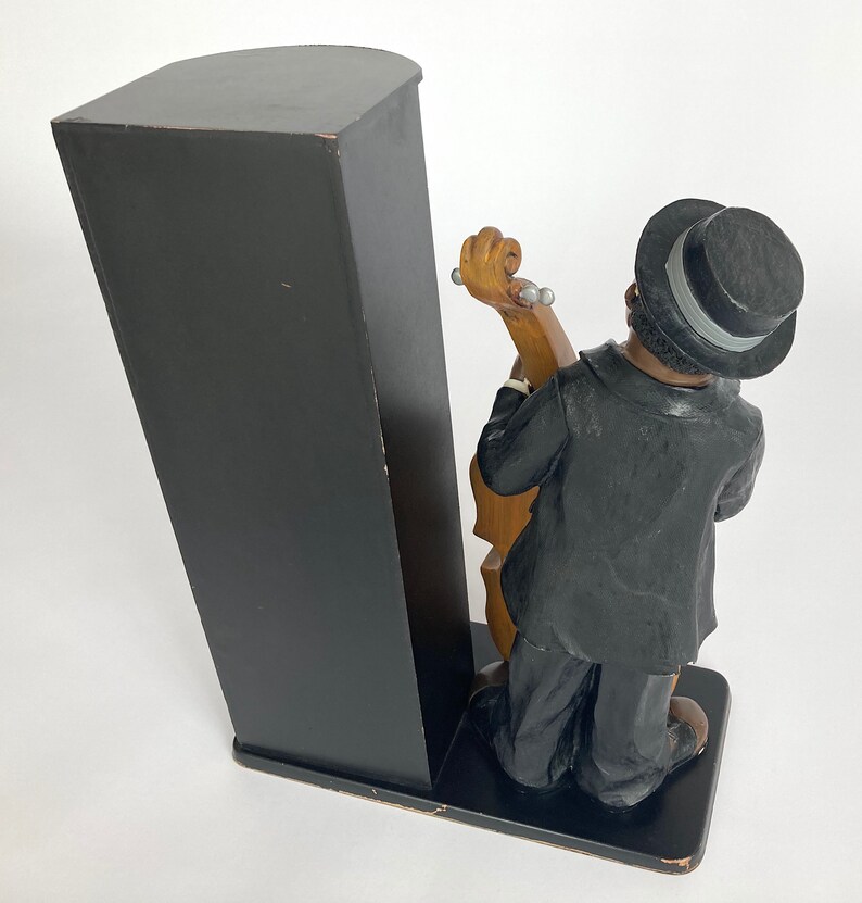 Pu&ograve; includere: Un fermacarte nero e marrone con una statuetta di un uomo in abito nero e cappello a cilindro che suona il basso.