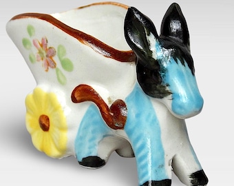 Könnte beinhalten: Eine kleine Keramikfigur eines Esels, der einen Miniaturwagen mit gelbem Blumendesign zieht. Der Esel ist in Blau, Schwarz und Weiß bemalt, und der Wagen ist weiß mit braunen Verzierungen und floralen Akzenten.