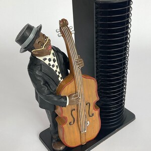 Pu&ograve; includere: Una torre per CD nera con una statuetta di un uomo che suona il basso. La statuetta &egrave; in resina ed &egrave; dipinta in nero, bianco e marrone. La torre per CD ha una finitura nera e pu&ograve; contenere fino a 50 CD.