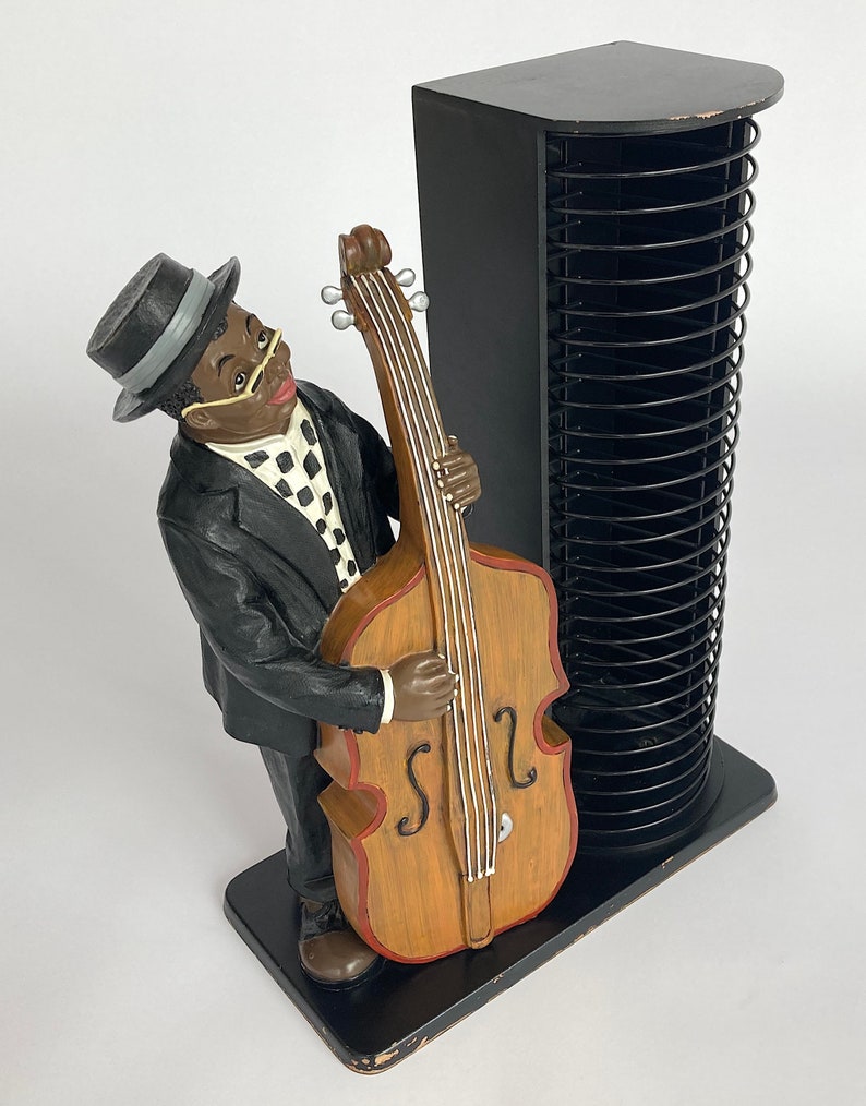 Pu&ograve; includere: Una torre per CD nera con una statuetta di un uomo che suona il basso. La statuetta &egrave; in resina ed &egrave; dipinta in nero, bianco e marrone. La torre per CD ha una finitura nera e pu&ograve; contenere fino a 50 CD.