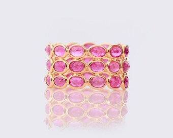 Könnte beinhalten: Ein goldener Ring mit drei Reihen rosafarbener ovaler Edelsteine.