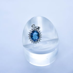 May include: A silver pendant with a blue oval gemstone surrounded by smaller clear gemstones.