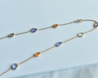 May include: A gold chain necklace with a variety of colorful gemstones. The stones are oval shaped and are set in a bezel setting. The necklace is approximately 18 inches long.