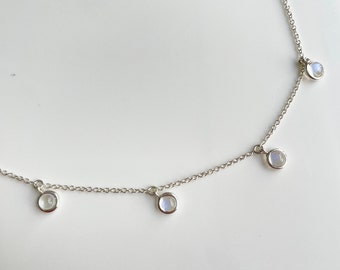 May include: A silver chain necklace with five small, round, white moonstone pendants.