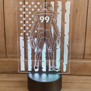 May include: A white acrylic night light with a silhouette of a football player wearing the number 99. The player is standing in front of an American flag design. The name "MALLADY" is at the top of the light.