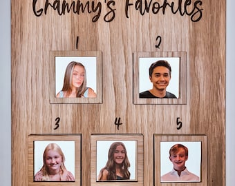 Puede incluir: Un tablero de madera con el texto "Grammy's Favorites" en la parte superior. Hay cinco marcos de fotos con los números del 1 al 5. Cada marco tiene una foto diferente de una persona.