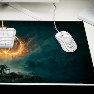 K&ouml;nnte beinhalten: Rechteckiges Gaming-Mauspad mit Fantasy-Landschaftsdesign, das einen Krieger und einen leuchtenden Ring zeigt. Eine wei&szlig;e Tastatur und Maus sind ebenfalls zu sehen. Das Mauspad liegt auf einem wei&szlig;en Schreibtisch.