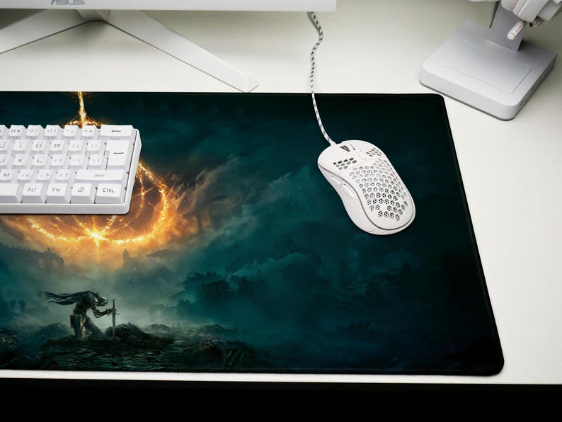 K&ouml;nnte beinhalten: Rechteckiges Gaming-Mauspad mit Fantasy-Landschaftsdesign, das einen Krieger und einen leuchtenden Ring zeigt. Eine wei&szlig;e Tastatur und Maus sind ebenfalls zu sehen. Das Mauspad liegt auf einem wei&szlig;en Schreibtisch.