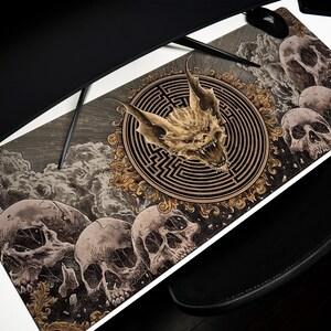 May include: A large rectangular mousepad featuring a detailed illustration. The design includes a central image of a bat-like creature within a circular maze, surrounded by skulls and ornate floral elements. The color palette is primarily grayscale with gold accents.