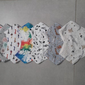 Peut inclure: Six bavoirs pour bébé avec différents motifs. Les bavoirs sont blancs avec des motifs colorés, notamment des notes de musique, des avions, des cœurs et un arc-en-ciel.