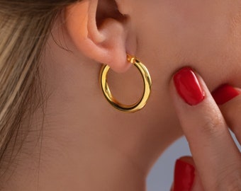 May include: A woman wearing gold hoop earrings. The earrings are thick and have a smooth, polished finish.