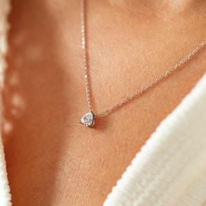 May include: A silver chain necklace with a single, clear, pear-shaped diamond pendant.