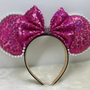 Puede incluir: Orejas de Minnie Mouse de lentejuelas rosas con un gran lazo rosa y ribete de perlas blancas.