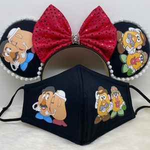 May include: A black face mask with a red, white, and blue bow headband. The mask features a cartoon image of Mr. and Mrs. Potato Head. The headband features a cartoon image of Mr. and Mrs. Potato Head on each ear.