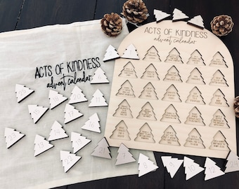 May include: A wooden advent calendar shaped like a Christmas tree with 25 numbered wooden tree ornaments. The calendar has the words "Acts of Kindness" and "Advent Calendar" written on it. Each ornament has a different act of kindness written on it.