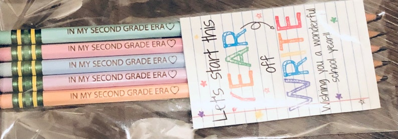 以下が含まれることがあります： 透明なビニール袋には、"IN MY SECOND GRADE ERA"の文字と小さなハートが付いた、パステルカラーの鉛筆が5本入っています。 "Let's start this YEAR off WRITE"という言葉が書かれたカードも含まれており、素晴らしい学校生活を願っています。