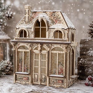 Puede incluir: Un modelo de casa de madera en miniatura con una estructura de dos pisos, ventanas arqueadas, una puerta central y una chimenea. El exterior está decorado con un patrón floral vintage y una ligera capa de nieve blanca en el techo y los bordes.