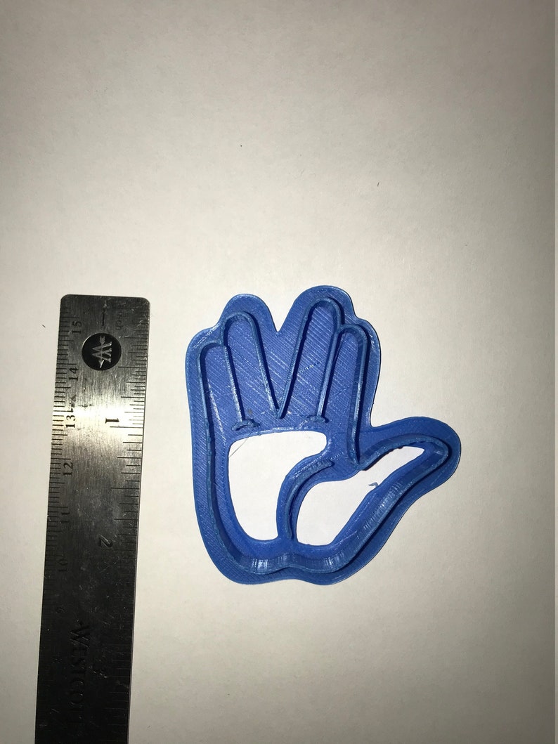 May include: A blue plastic cookie cutter shaped like a hand with four fingers raised in a Vulcan salute. The cookie cutter is about 2 inches wide.