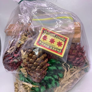 May include: A clear plastic bag filled with brown shredded paper, three pine cones, one green pine cone, and a box of matches. The matchbox is red and yellow with the text "Three Stars" and "Safety Matches".