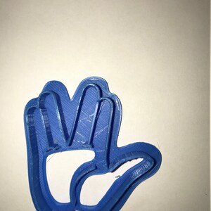 May include: A blue plastic cookie cutter shaped like a hand with five fingers. The cookie cutter is designed to cut out cookies in the shape of a hand.