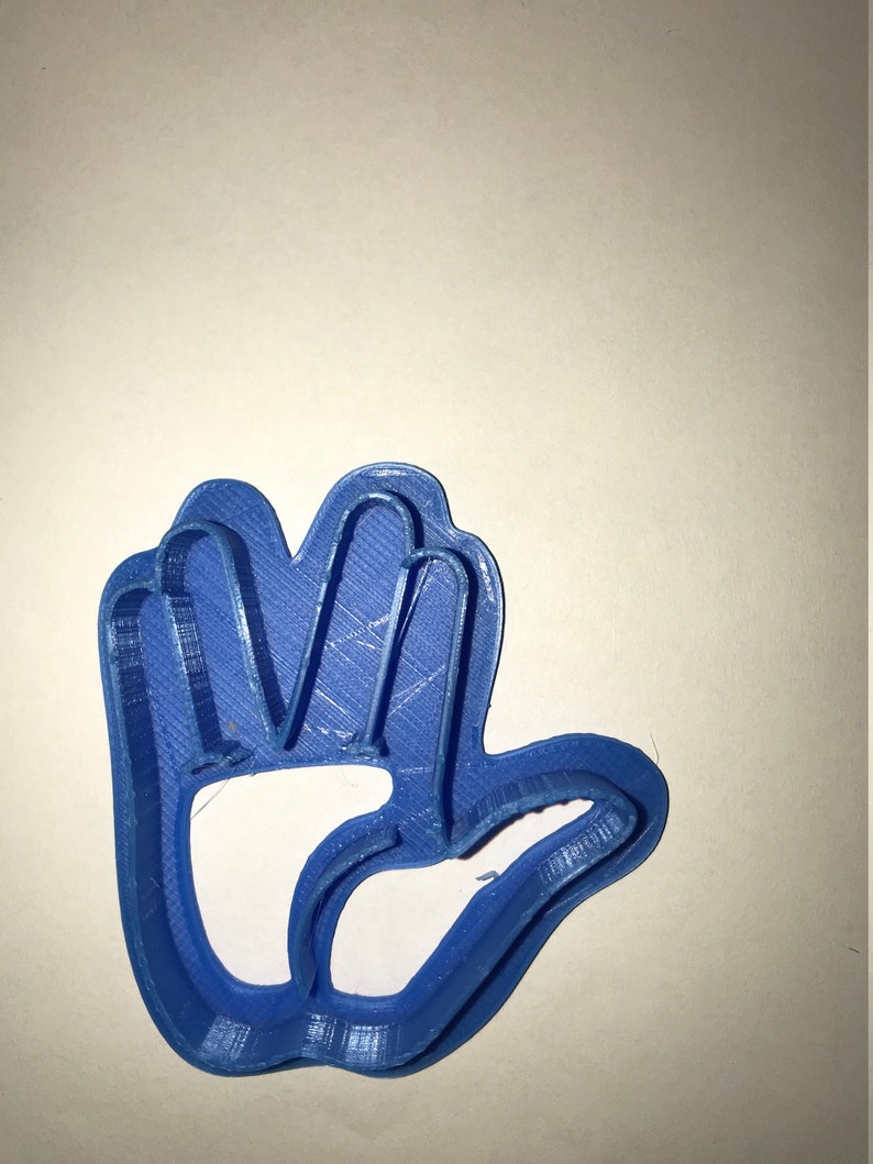 May include: A blue plastic cookie cutter shaped like a hand with five fingers. The cookie cutter is designed to cut out cookies in the shape of a hand.