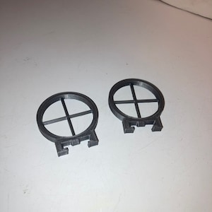 May include: Two black plastic rings with a cross-shaped design. The rings have four small tabs on the bottom.
