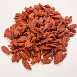 May include: A pile of dried goji berries, also known as wolfberries, on a white background. The berries are a deep red color and have a slightly wrinkled texture.