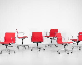 Peut inclure: Six chaises de bureau rouges avec des cadres argentés et des bases roulantes sont disposées sur un fond blanc. Les chaises ont un design bas avec des accoudoirs. Les chaises sont de style moderne et minimaliste.