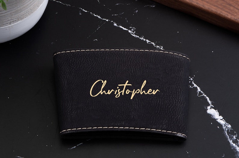 Puede incluir: Funda para taza de caf&eacute; de cuero negro con un borde cosido dorado y el nombre "Christopher" escrito en letras doradas.