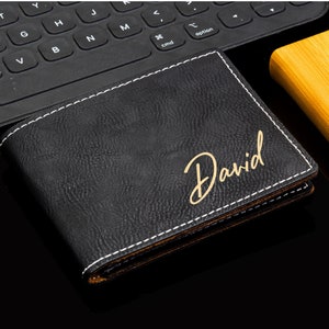 Puede incluir: Una cartera de cuero negro con costuras blancas y una inscripci&oacute;n dorada que dice "David".