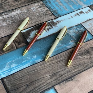 May include: Four wooden pens with gold accents. Two pens are brown and two pens are cream colored.