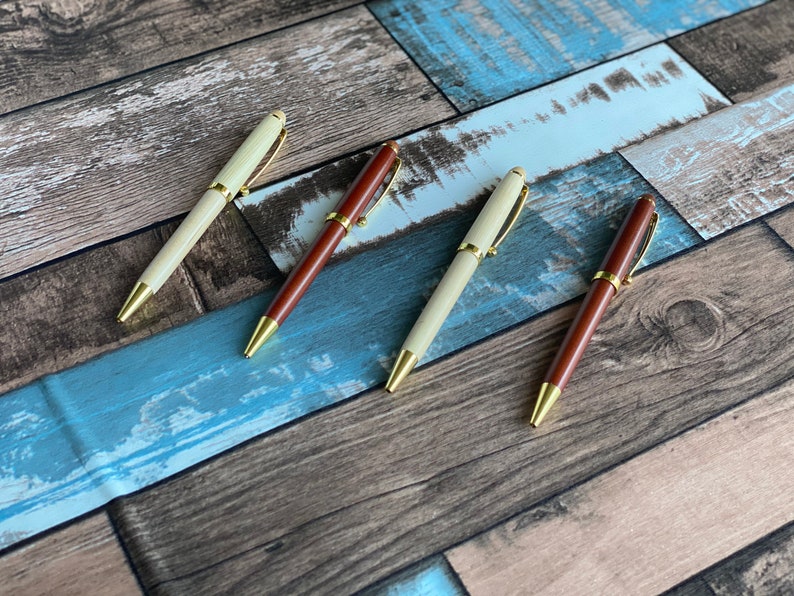 May include: Four wooden pens with gold accents. Two pens are brown and two pens are cream colored.