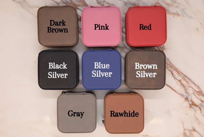 Puede incluir: Nueve cajas de joyer&iacute;a cuadradas en diferentes colores, incluyendo marr&oacute;n oscuro, rosa, rojo, negro, azul, marr&oacute;n, gris y cuero crudo. Cada caja tiene un color diferente y una etiqueta con el nombre del color.