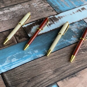 May include: Four pens with gold accents and wooden barrels. Two pens are light brown and two pens are dark brown.