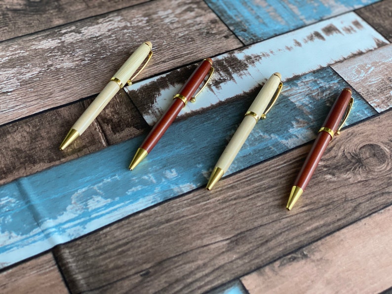 May include: Four pens with gold accents and wooden barrels. Two pens are light brown and two pens are dark brown.