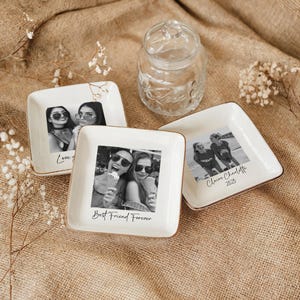 May include: White square ceramic trinket dishes with gold trim, each featuring a black and white photograph. One dish reads "Love you", another "Best Friend Forever", and a third "Claire Charlotte 2025". A clear glass jar is in the background.