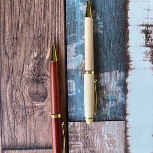 May include: Two wooden pens with gold accents. One pen is brown and the other is light wood.