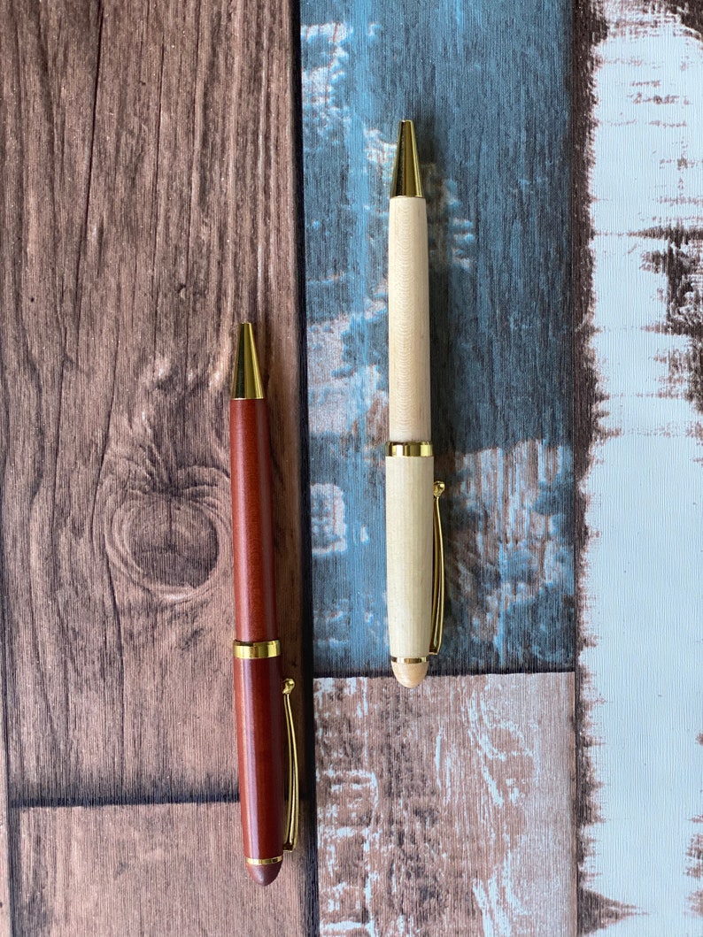May include: Two wooden pens with gold accents. One pen is brown and the other is light wood.
