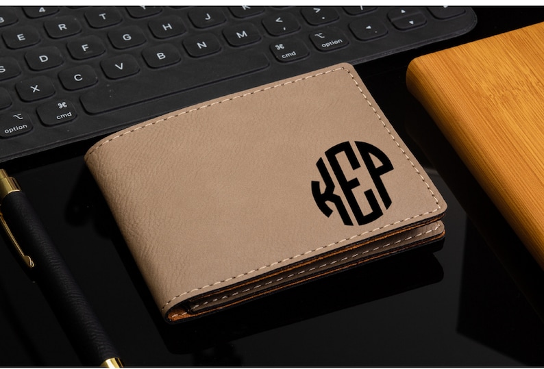 May include: A tan leather wallet with a brown stitched edge. The wallet has a black circle monogram with the letters "K.E.P."