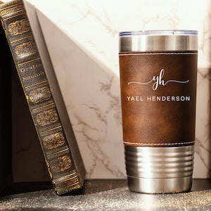 May include: A brown leather-wrapped stainless steel tumbler with a white monogram "yh" and the name "Yael Henderson" engraved on the front.