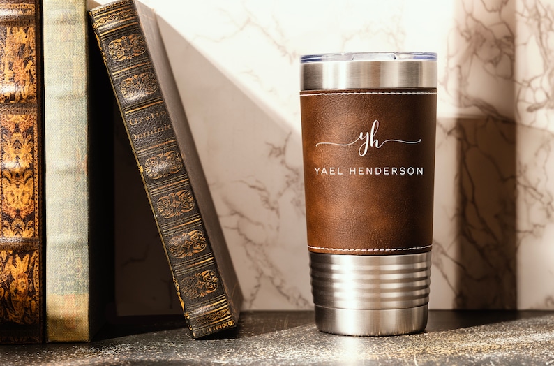 May include: A brown leather-wrapped stainless steel tumbler with a white monogram "yh" and the name "Yael Henderson" engraved on the front.