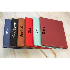May include: Six leather-bound journals in different colors, including blue, black, brown, red, teal, and rose. Each journal has a color-coordinated stitching detail and a title embossed on the front cover.