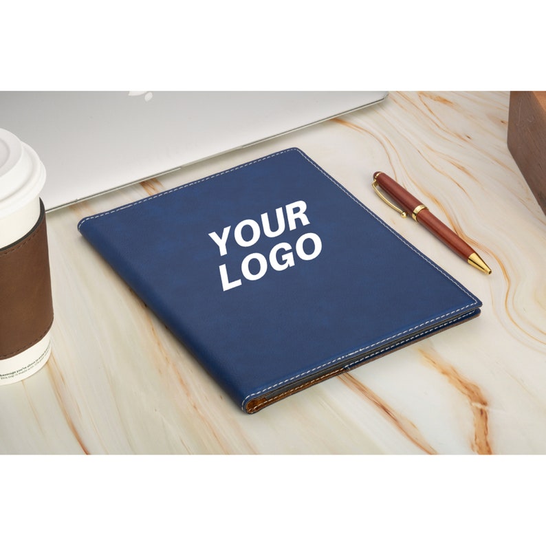 May include: A blue leather notebook with a brown leather trim and the text "YOUR LOGO" printed in white on the cover.