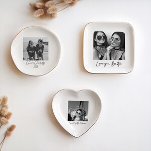 May include: Three white ceramic trinket dishes with gold rims. Each dish features a black and white photograph. One is round, one square, and one heart-shaped. Text on the dishes reads "Claire Charlotte 2025", "Love you Bestie", and "Soul Sister Forever".