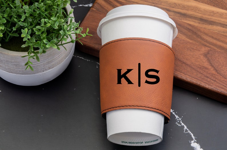 Puede incluir: Una funda de taza de caf&eacute; de cuero marr&oacute;n con las iniciales "K|S" en letras negras.