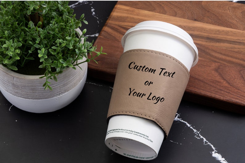 Puede incluir: Una funda de taza de caf&eacute; de cuero marr&oacute;n con el texto "Custom Text or Your Logo" impreso en ella.