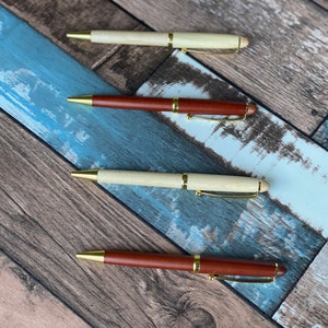 May include: Four wooden pens with gold accents. Two pens are brown and two pens are light wood.