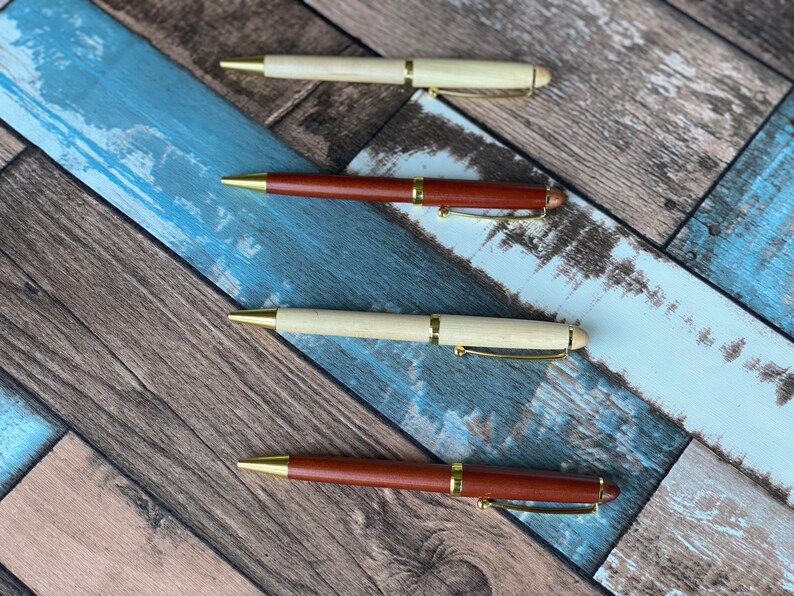 May include: Four wooden pens with gold accents. Two pens are brown and two pens are light wood.