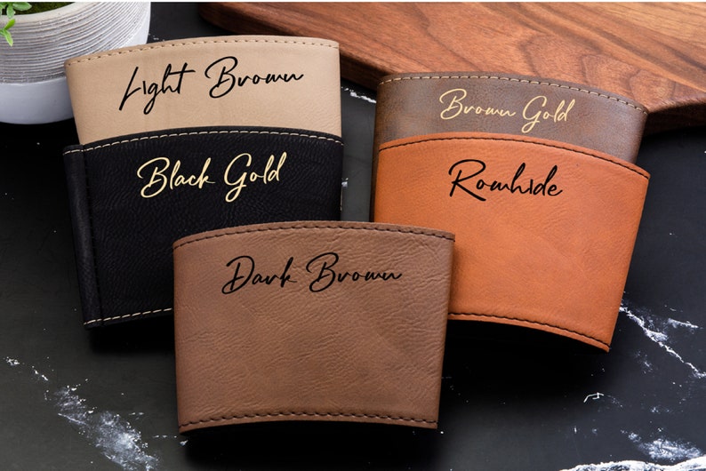 Puede incluir: Cuatro portavasos de cuero de diferentes colores con letras doradas. Los colores son marr&oacute;n claro, negro, marr&oacute;n dorado y marr&oacute;n oscuro. Las letras dicen "Light Brown", "Black Gold", "Brown Gold", y "Dark Brown".